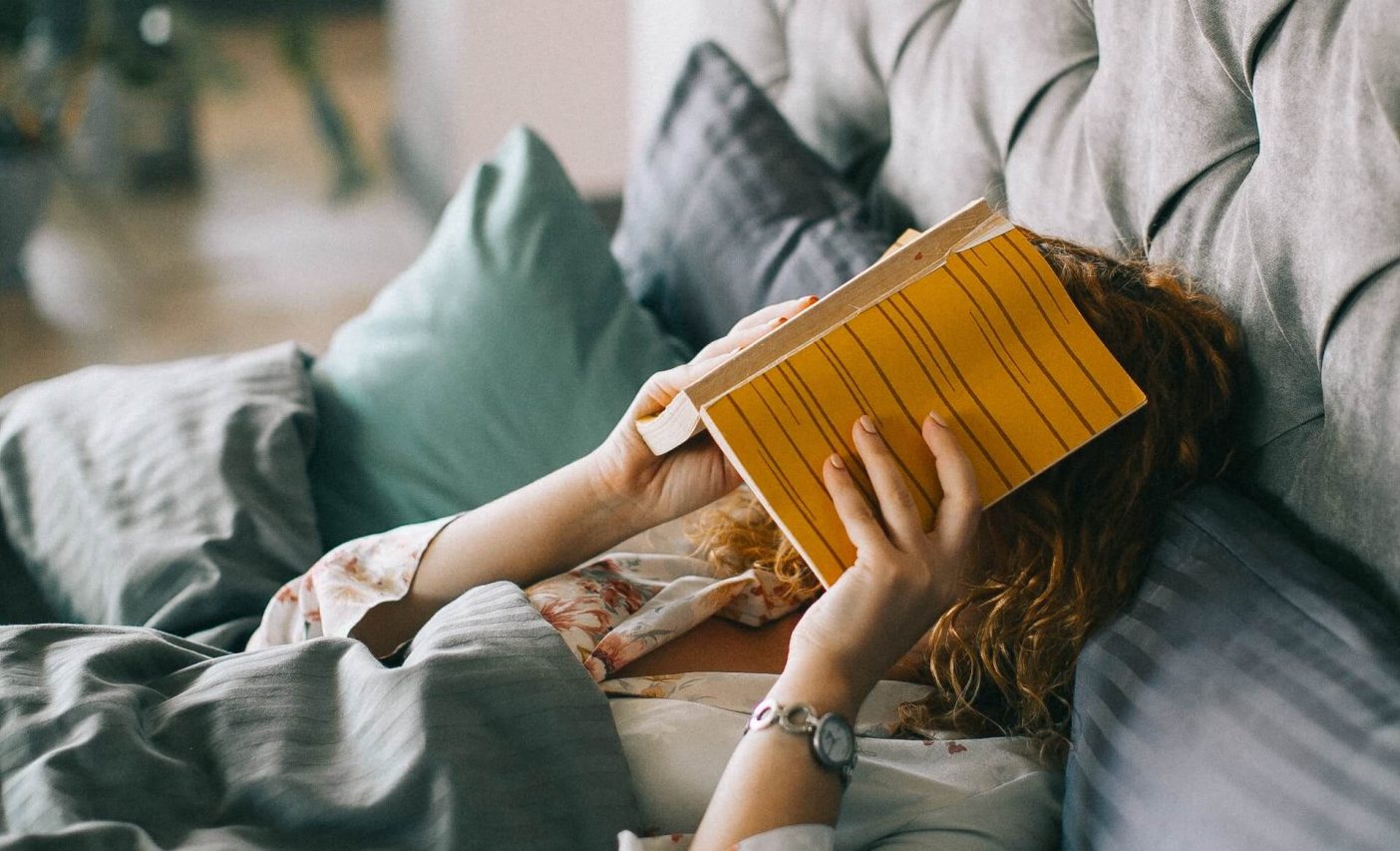 Frau bedeckt ihr Gesicht mit einem Buch auf dem Bett 1404x853 1